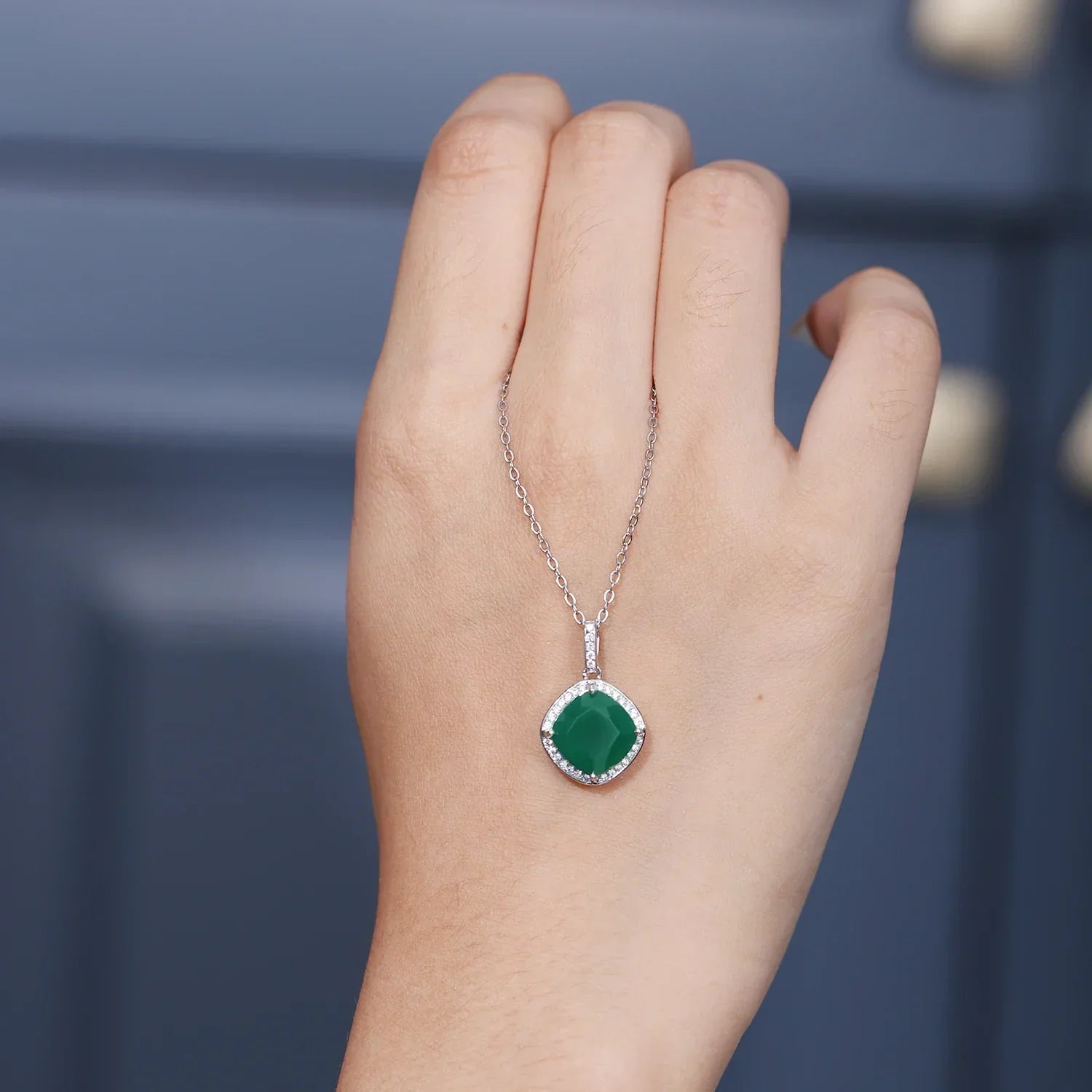 Hand holding Rosary Milano necklace with green gemstone pendant and silver chain